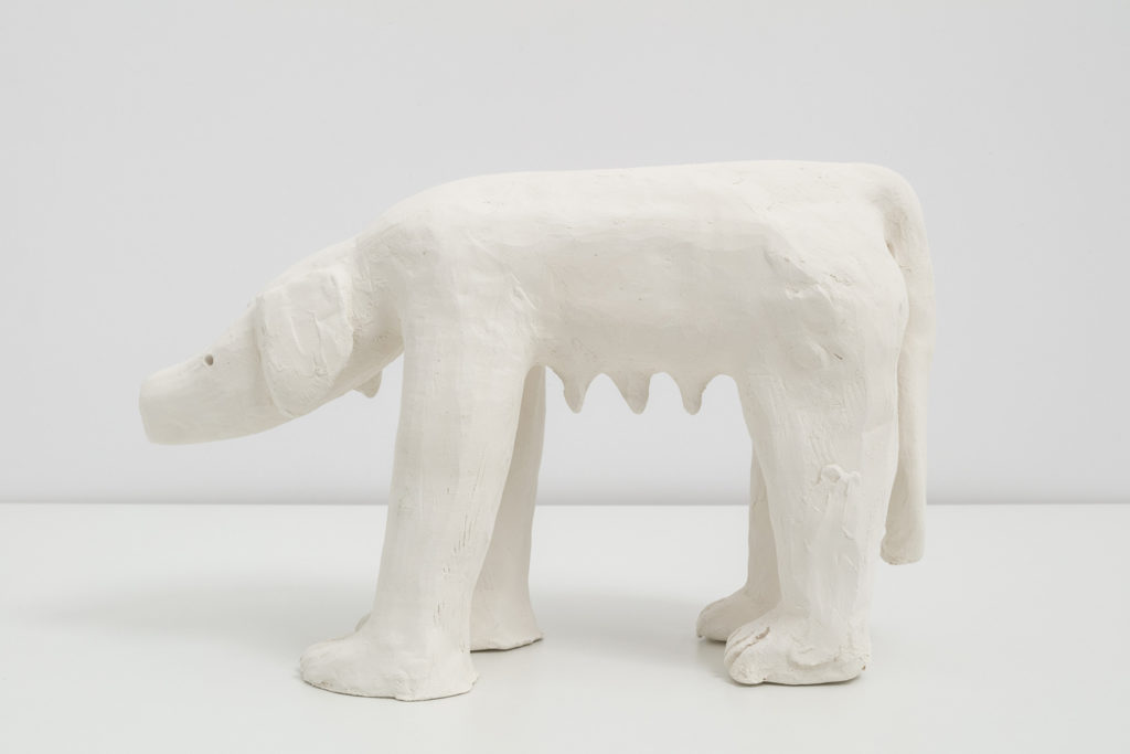 An off white ceramic sculpture of a labrador dog on all fours, but her front legs are human arms and hands.