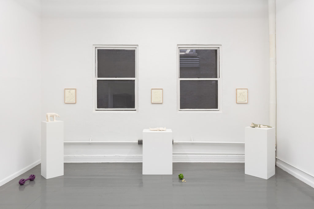 An installation view showing three small ballpoint pen drawings, three pedestals with small ceramic animal sculptures, and two dog toy sculptures on the floor.