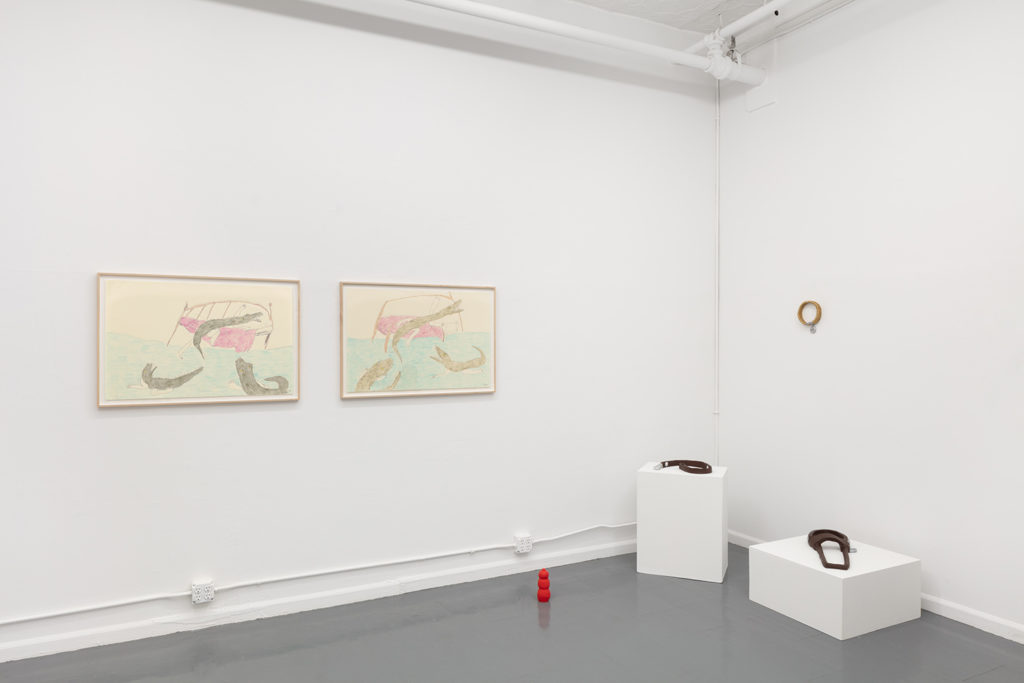 An installation view showing two Alligatorgirl drawings side-by-side and four ceramic sculptures of dog gear and toys - displayed on pedestals, the wall, and the floor.