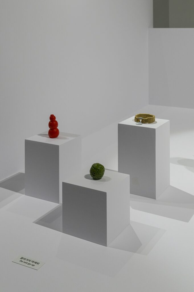 In this vertical installation shot from "Seeing With 10 Fingers", "Kong", "Green Ball", and "Golden Dog Collar" are installed on three adjacent white plinths of varying heights.