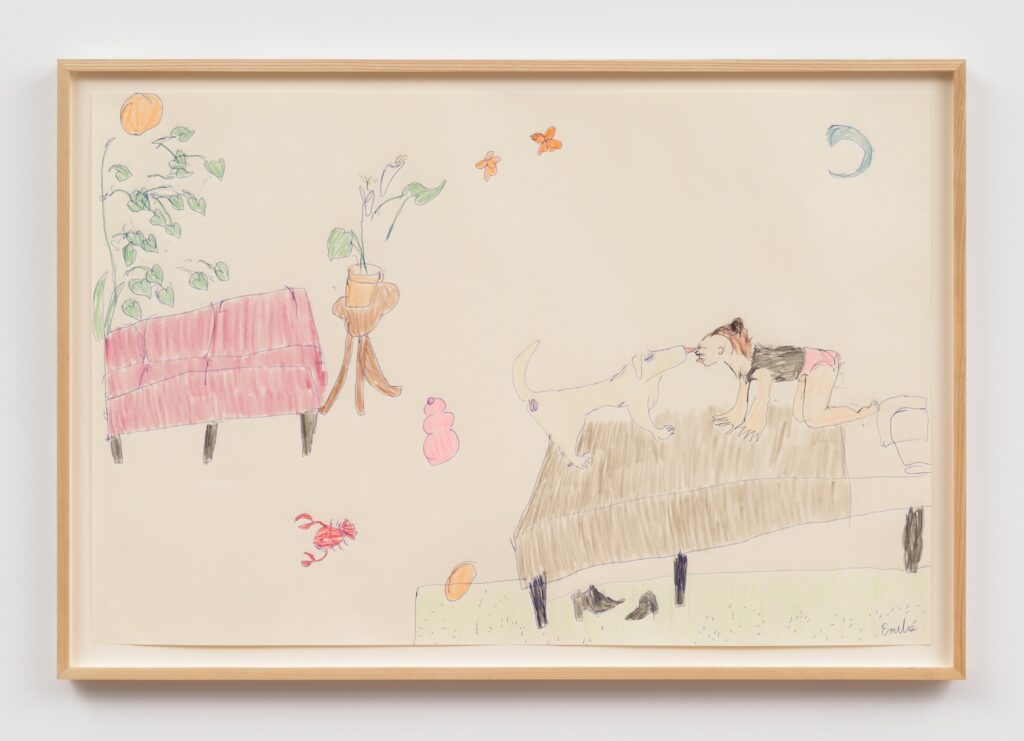 “Playing in Bed (with lobster)” is a colorful drawing on off-white paper, framed in a light wood frame. On the left side of the drawing, a burgundy couch with four brown legs, drawn with visible lines to indicate cushions. Behind the couch, a tall green plant with heart-shaped leaves grows upward, with a round orange sun peeking through the green leaves. Next to the couch, a small round table with three legs holds a potted plant. The plant has two large green leaves and a single purple flower. Below the table, a pink Kong chew toy sits on the floor. Near the bottom left, a small red lobster is drawn with a round body and extended claws. In the center and right: A large brown bed, sits on four legs. On the bed, Emilie with brown hair in a bun, wearing a black tank top and pink underwear, is on all fours, facing London, a blonde English Labrador Retriever. Their faces are close together with their tongues affectionately licking each other, as if French kissing. London is drawn with a long tail. Under the bed, two black ankle boots rest on top of a green rug. In front of the bed, an orange ball sits on a patch of green carpet. In the background, two orange butterflies are drawn in the air above Emilie and London. A blue crescent moon is in the upper right corner.