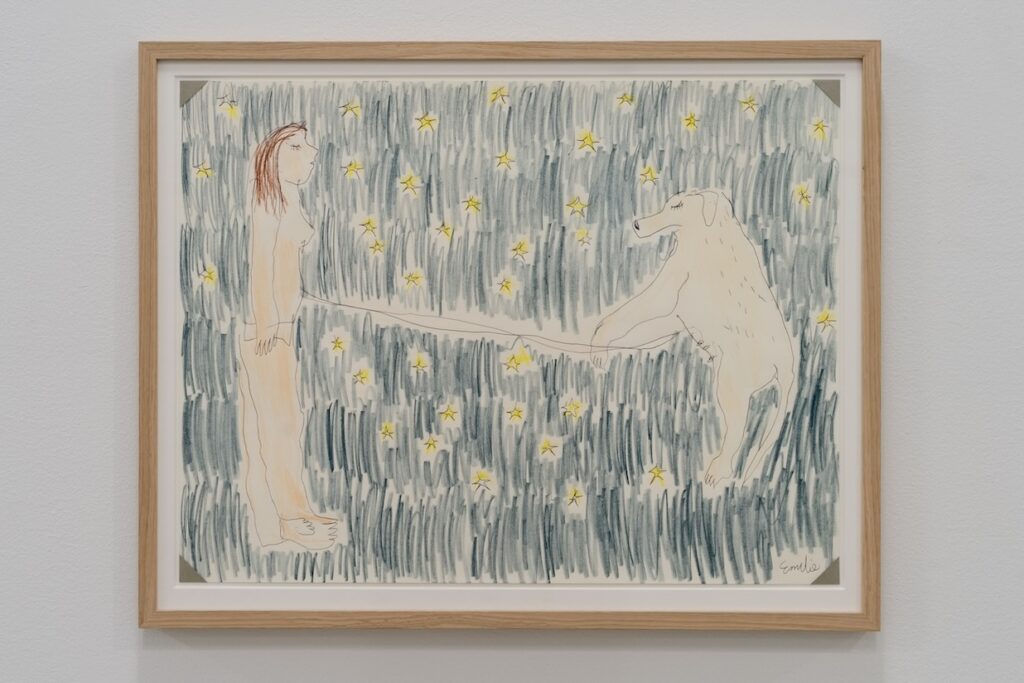 "Dogs and Humans Figure a Universe" is a colored drawing on white paper slightly larger than a cookie tray. The drawing is framed in oak. It shows Emilie and London floating together in an inky black cosmic night sky scattered with bright yellow stars. Emilie and London face each other, connected by an umbilical cord, symbolizing a deep, mother-child-like bond.