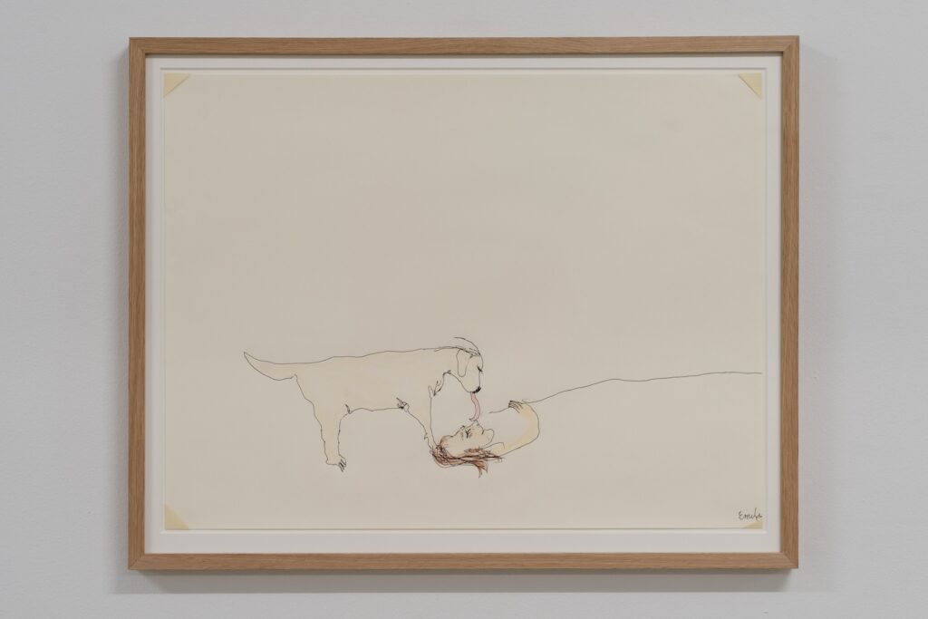 "Good Morning" is a colored drawing on white paper slightly larger than a cookie tray. The drawing is framed in oak. Created with ballpoint pen and crayon, the artwork features Emilie's head and her long brown hair peeking out from beneath a thin black line drawn across the page from her chin that suggests a blanket. London, whose blonde body extends across the opposite side of the page, stands over Emilie, with their heads positioned on top of each other. London's long, bright red tongue dangles down from her mouth, reaching out to give Emilie a warm lick to wake Emilie up.