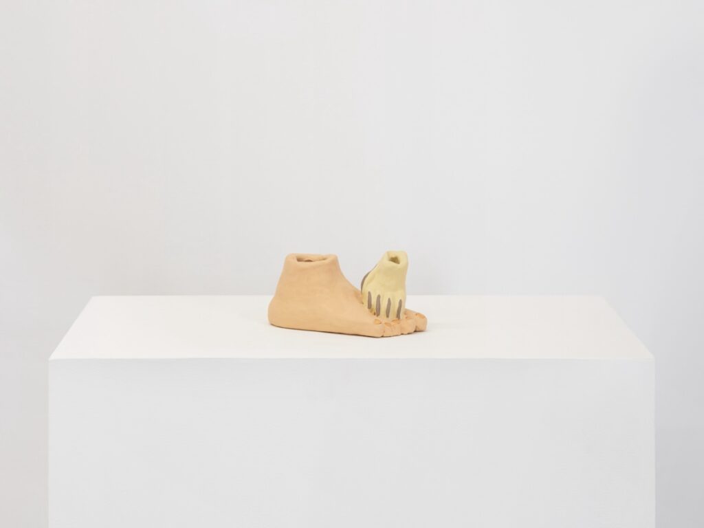 "Paw on Foot" is a painted ceramic sculpture depicting a human foot, cutoff at the ankle, with a blond dog paw, also cutoff at the ankle, resting on top of it. The paw presses directly into the fleshy part of the foot right behind the toes. There is a real intimacy to this pose.